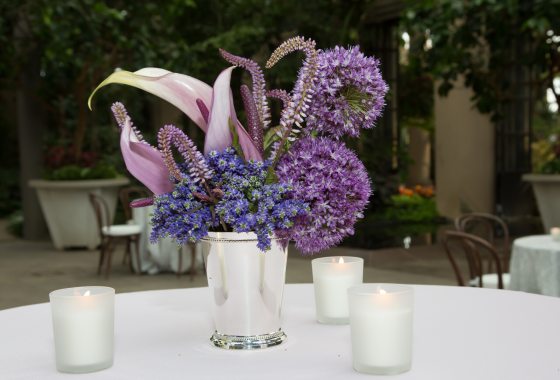 A silver vase filled with purple blooming flowers on a white tablecloth.